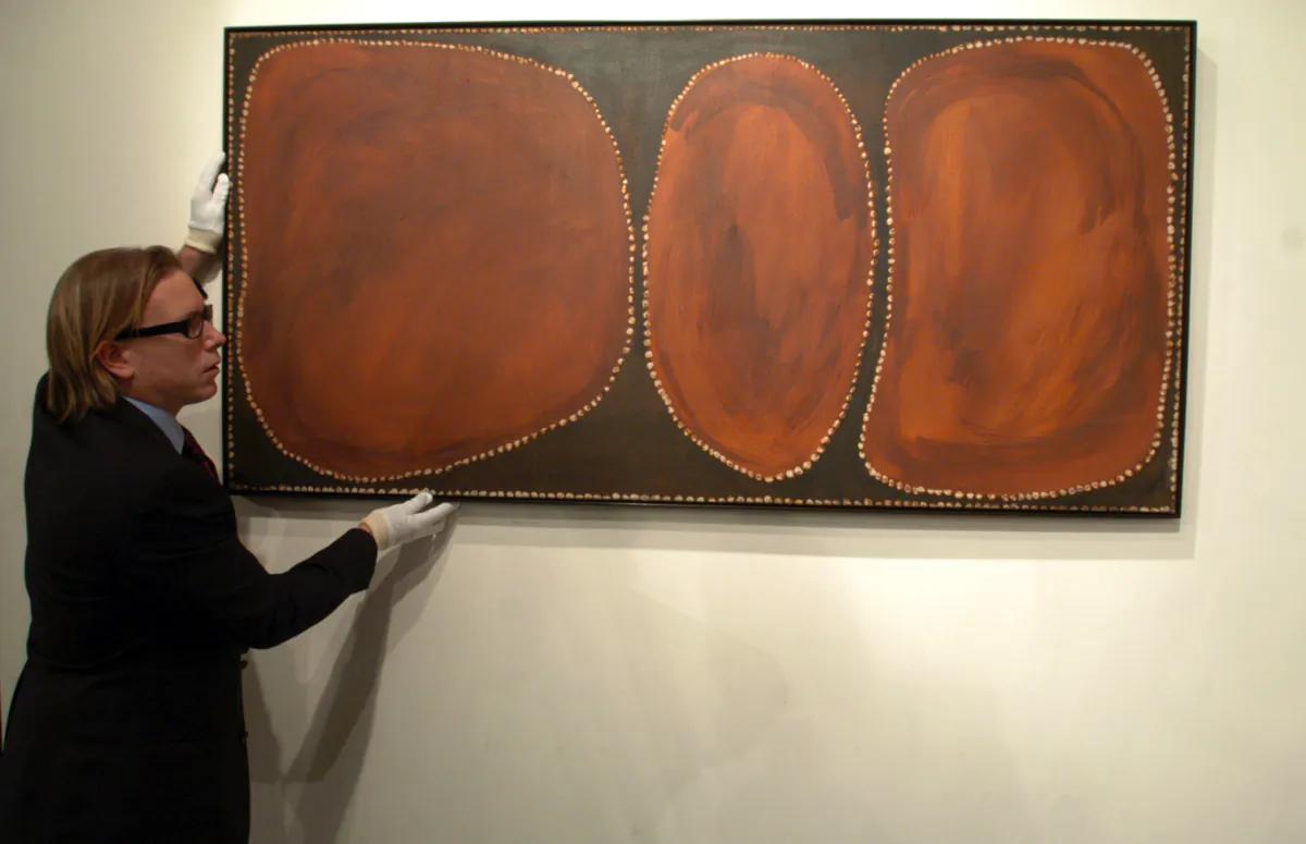  Tim Klingender, director of Aboriginal Art at Sotheby's Australia, straightens the painting "Uluru" (1967) by Rover Thomas at Sotheby's in Melbourne, on July 26, 2004. (AAP Image/Julian Smith)
