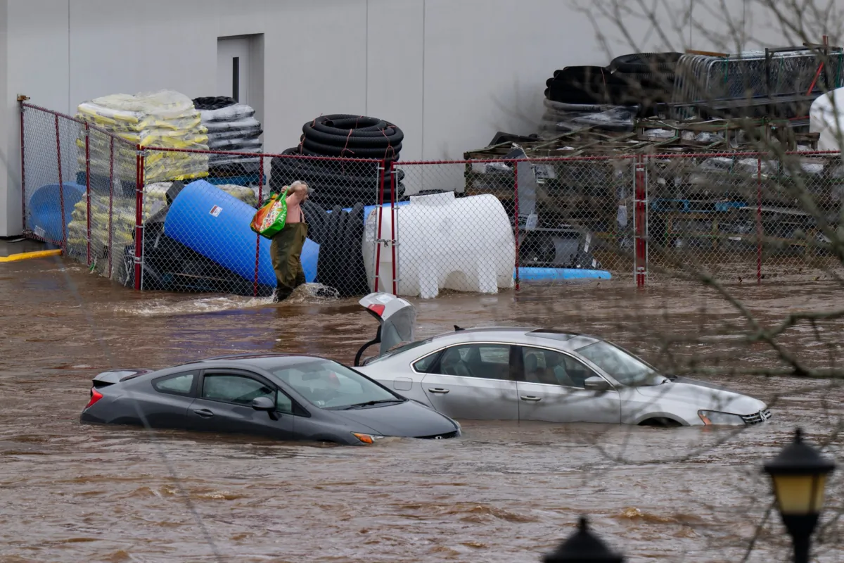A man wearing chest waders walks past cars abandoned in floodwater in a mall parking lot following a major rain event in Halifax on Saturday, July 22, 2023. (Darren Calabrese/The Canadian Press)