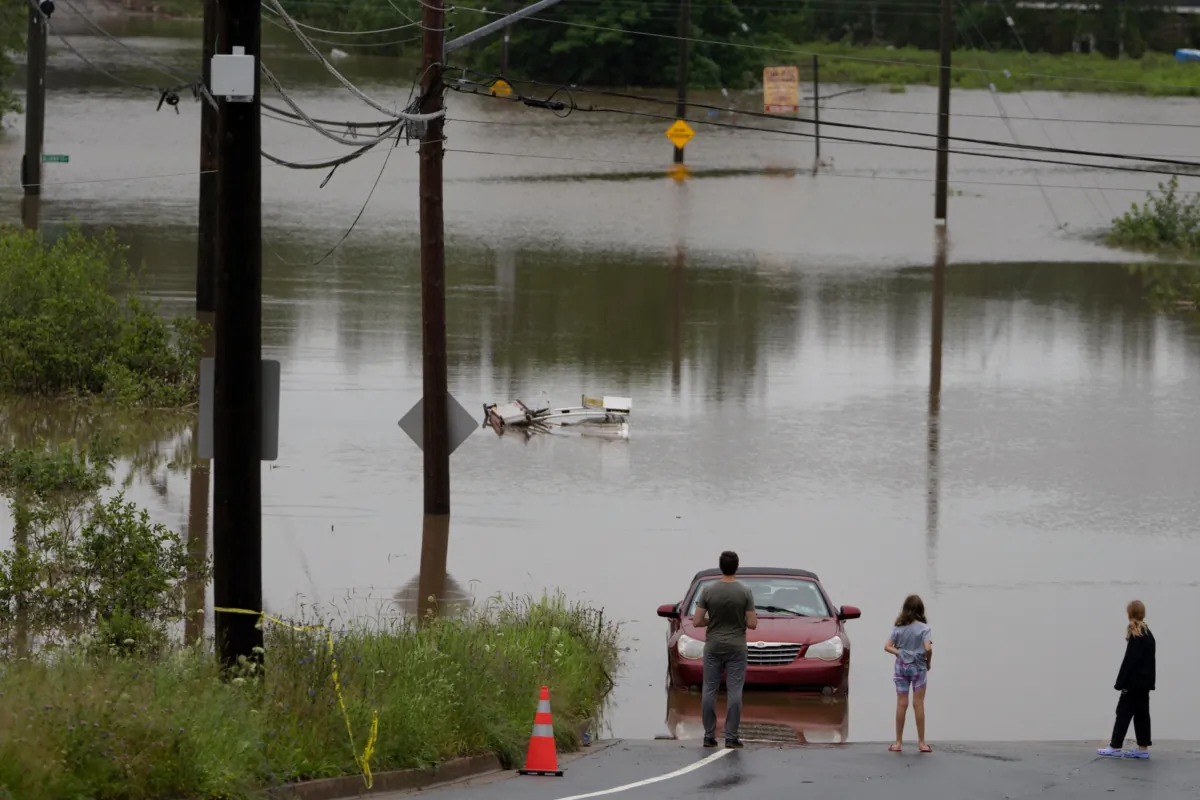 People stand at the edge of floodwater as vehicles are seen abandoned in water following a major rain event in Halifax on Saturday, July 22, 2023. (Darren Calabrese/The Canadian Press)