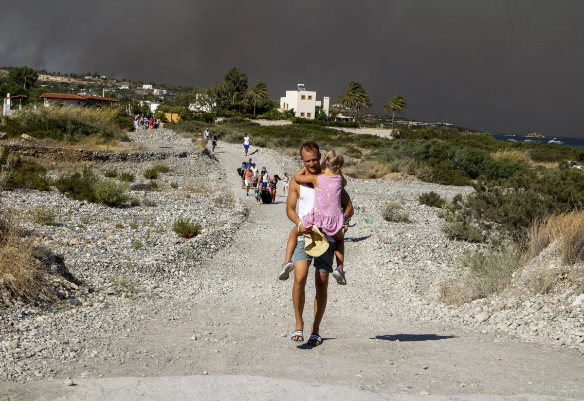 A man carries a child as they leave an area where a forest fire burns, on the island of Rhodes, Greece, on July 22, 2023. (Lefteris Diamanidis/InTime News via AP)