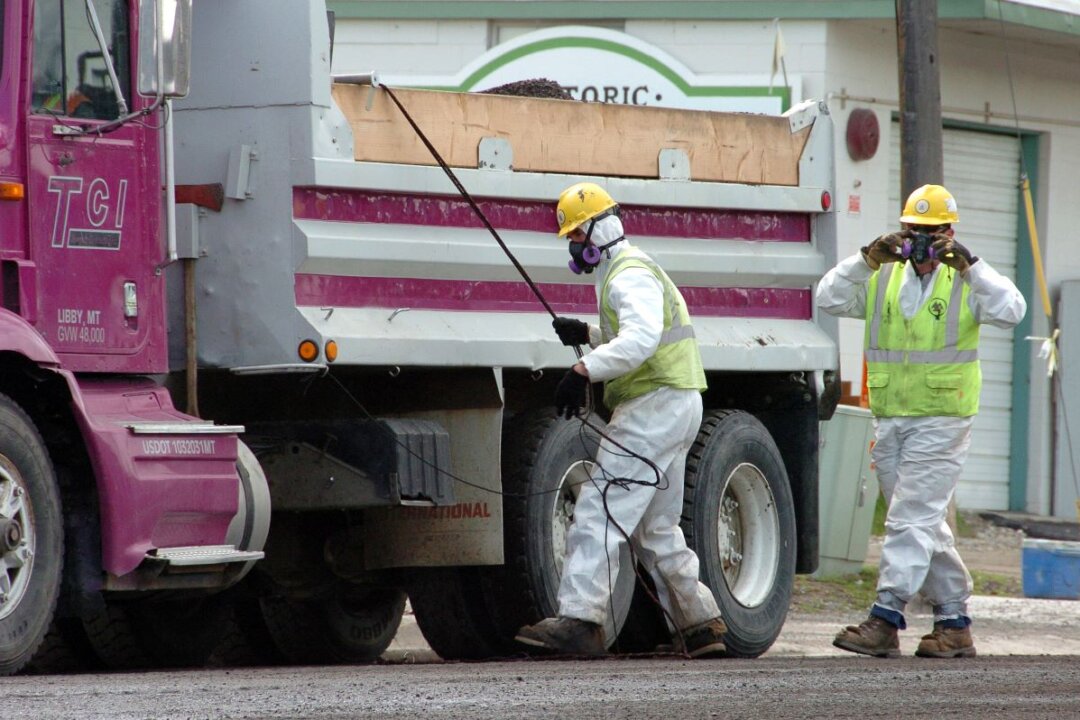 Unidentified road workers wear protective gear against possible asbestos contamination as they load material from a road resurfacing project in downtown Libby, Mont., on April 28, 2011. (Matthew Brown/AP)