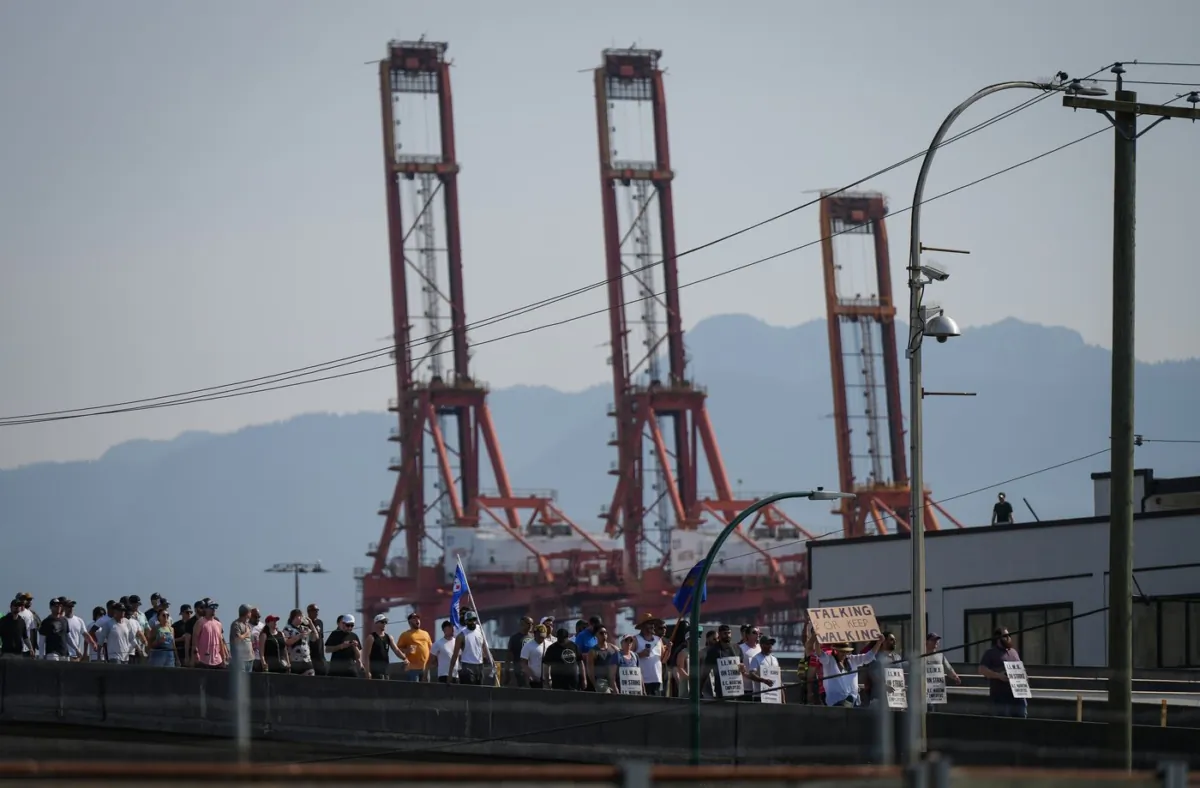 Striking International Longshore and Warehouse Union Canada workers march to a rally as gantry cranes used to load and unload cargo containers from ships sit idle at port in Vancouver on July 6, 2023. (The Canadian Press/Darryl Dyck)