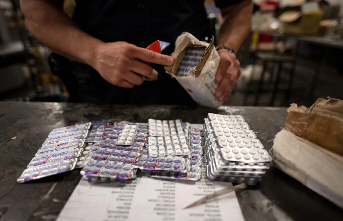 An officer from the U.S. Customs and Border Protection, Trade and Cargo Division finds Oxycodone pills in a parcel at John F. Kennedy Airport's US Postal Service facility in New York on June 24, 2019. (Johannes Eisele/AFP via Getty Images)