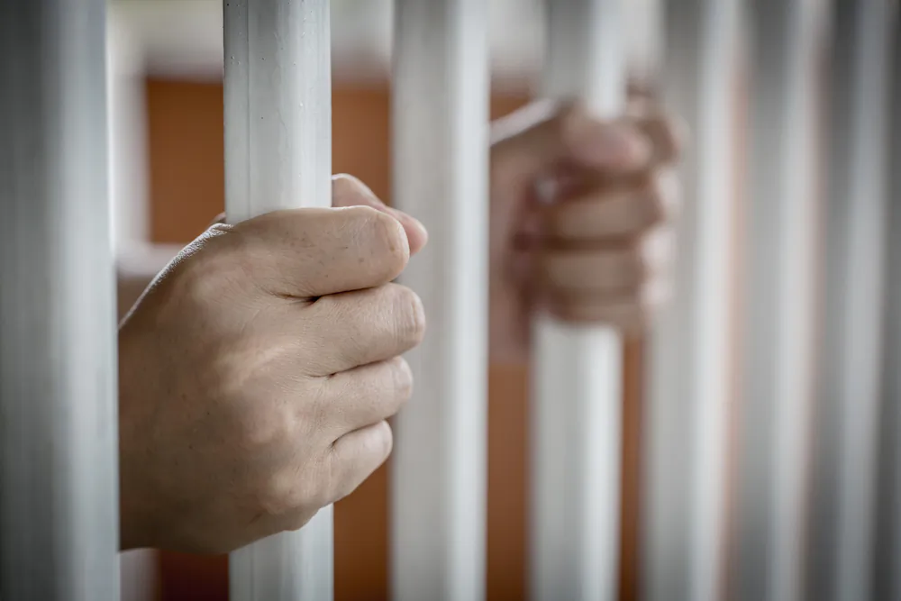 Hands of Asian prisoner behind the jail (Shutterstock)