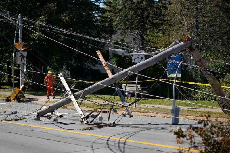 A worker walks past downed power lines and a pole caused by post-tropical storm Fiona in Dartmouth, N.S. on Sept. 25, 2022. (The Canadian Press/Darren Calabrese)