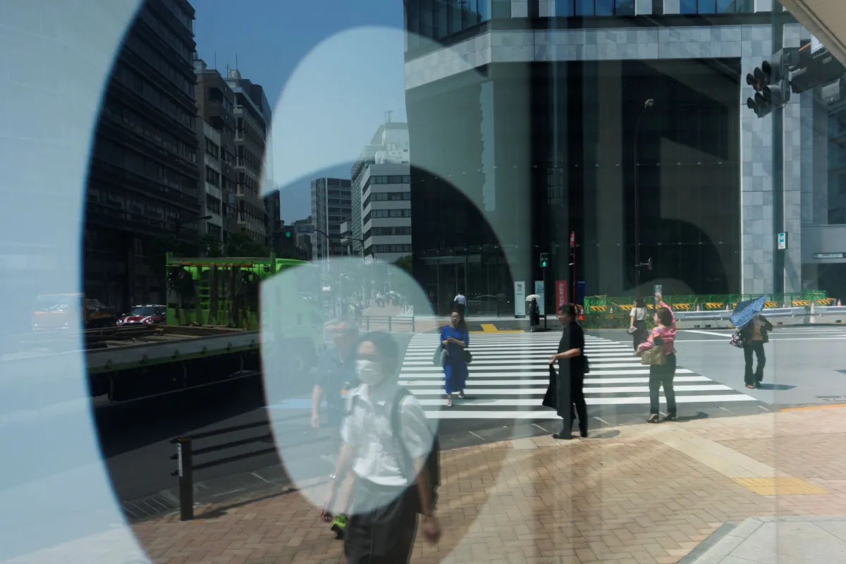 People walk across an intersection near monitors showing Japan's Nikkei 225 index at a securities firm in Tokyo, Japan, on July 27, 2023. (Hiro Komae/AP Photo)