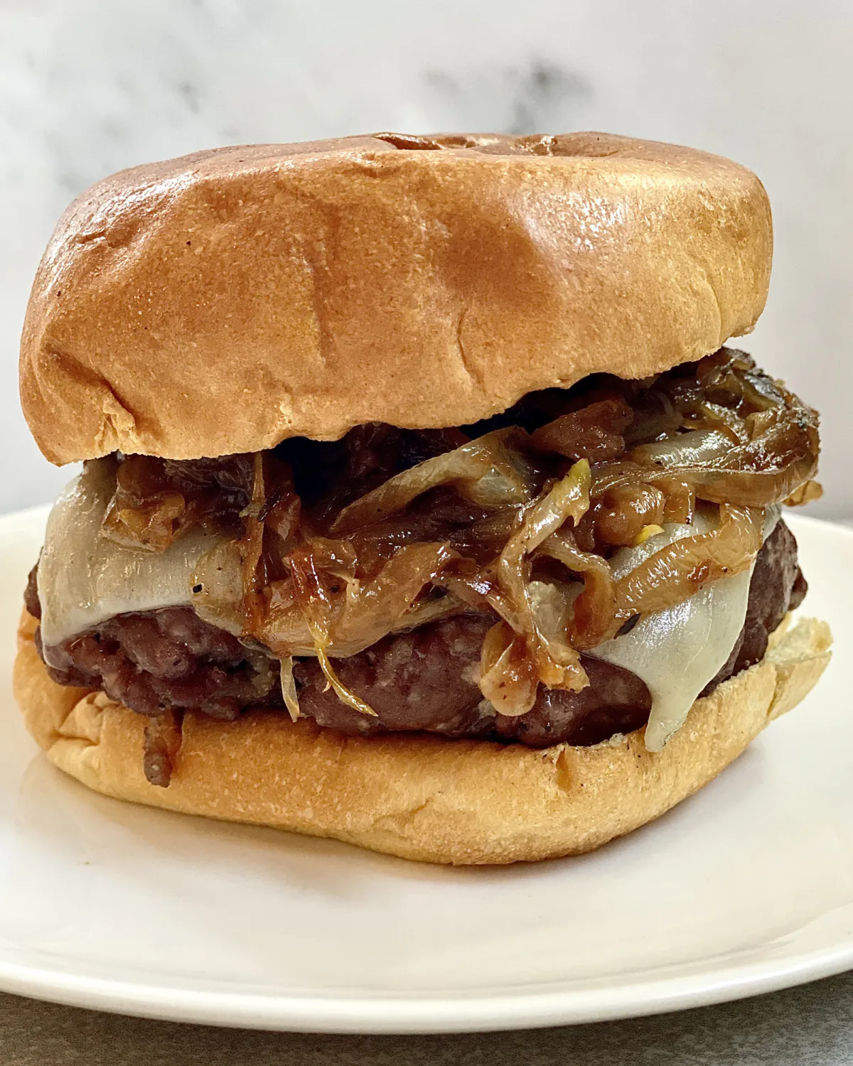 These grilled hamburgers are piled high with caramelized onions and melty Gruyere cheese. (Kelli Foster/TNS)