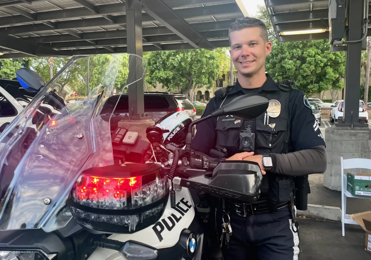 Irvine Police Officer Tyler Hollenbeck poses next to a motorcycle at the "National Night Out" at Woodbury Community Park in Irvine, Calif., on Aug. 1, 2023. (Carol Cassis/The Epoch Times)