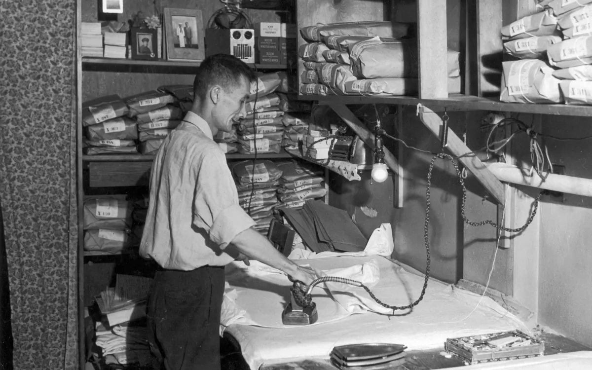 A laundry worker irons a shirt with shelves around him holding cleaned clothes wrapped in brown paper, circa 1945. (Lawrence Thornton/Getty Images)