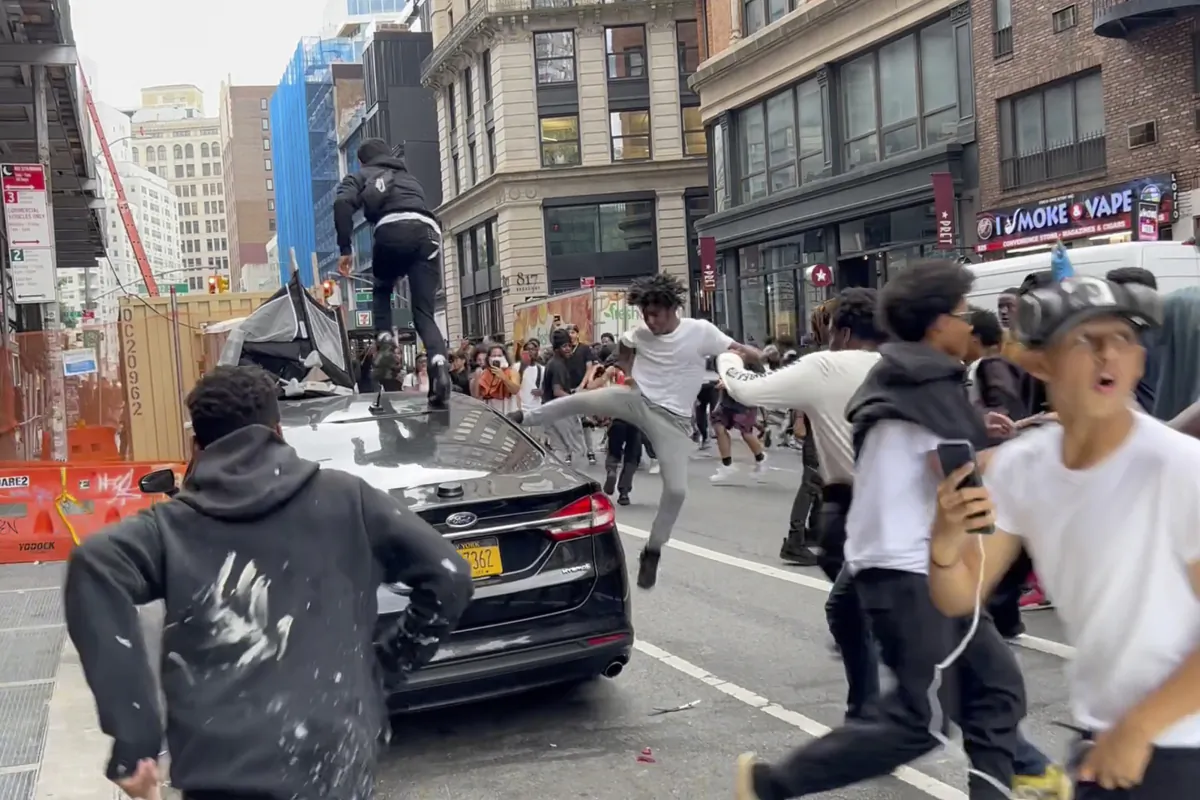 In this photo taken from video, people jump and kick a car as a crowd runs through the street on Broadway near Union Square in New York, on Aug. 4, 2023. (AP Photo/Bobby Calvan)