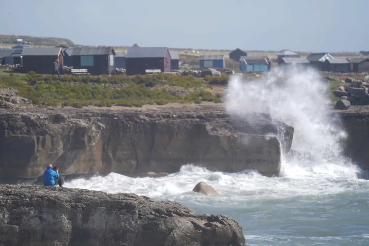 A man photographs waves crashing against the shore in Portland, Dorset, on Aug. 5, 2023. (James Manning/PA)