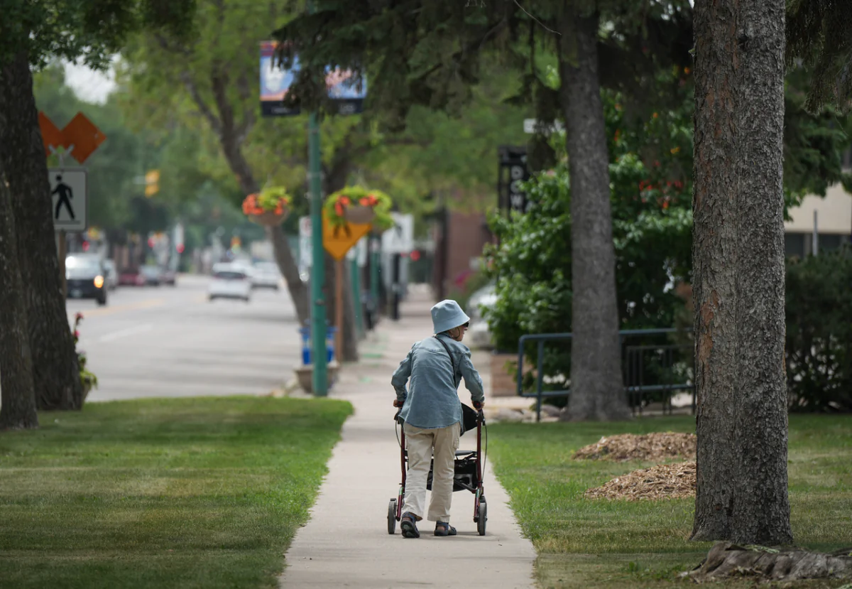An elderly woman uses a rollator walker while out for a walk along Main Street, in Dauphin, Manitoba, on June 17, 2023. (Darryl Dyck/The Canadian Press)