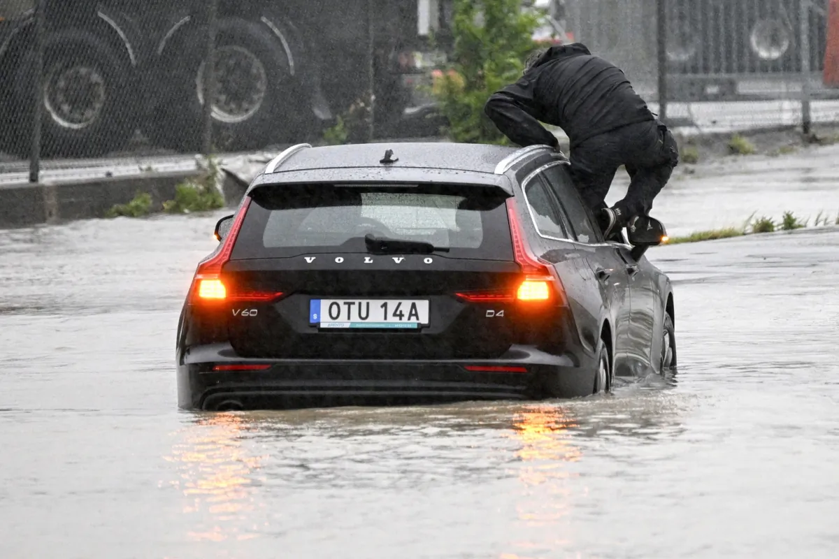 A man climbs out of a car which got stuck at a flooded roundabout in Arlöv, along the E6 road outside Malmö, southern Sweden, on Aug. 7, 2023. (Johan Nilsson/TT News Agency via AP)