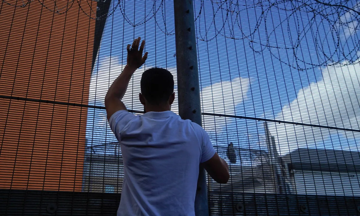A protester communicates with those inside at the perimeter fence of Brook House immigration removal centre beside Gatwick Airport, south of London on June 12, 2022. (Niklas Halle'n/AFP via Getty Images)