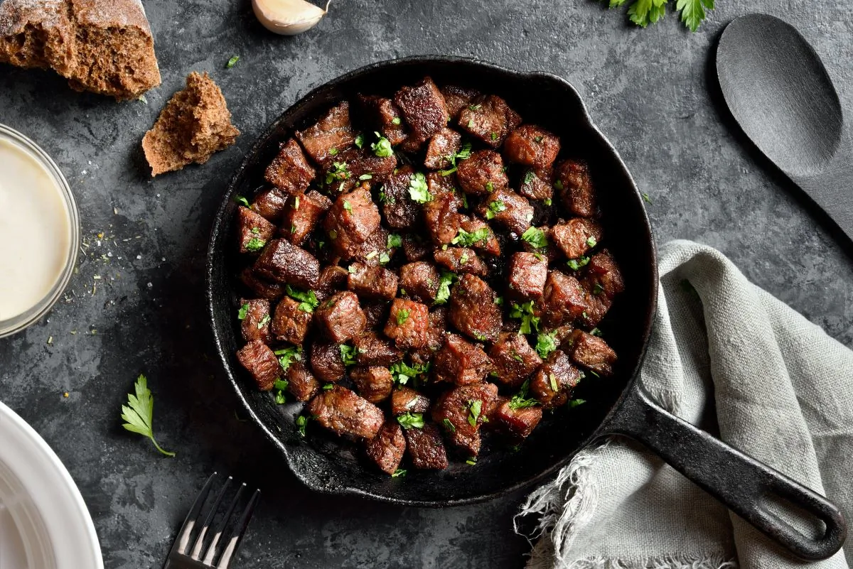 Garlic butter steak bites in cast iron pan over dark stone background. (Tatiana Volgutova/Shutterstock)