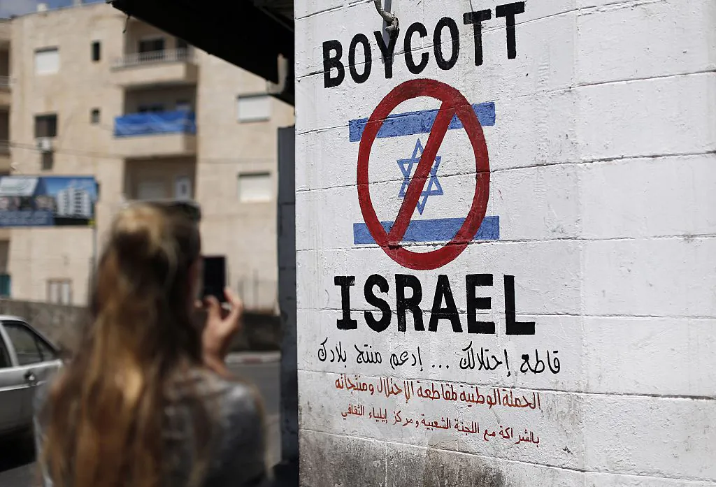 A tourist photographs a sign on a wall in the West Bank biblical town of Bethlehem on June 5, 2015, calling to boycott Israeli products coming from Jewish settlements. The international BDS (boycott, divestment and sanctions) campaign, that pushes for a ban on Israeli products, aims to exert political and economic pressure over Israel's occupation of the Palestinian territories in a bid to repeat the success of the campaign that ended apartheid in South Africa. (Thomas Coex/AFP via Getty Images)