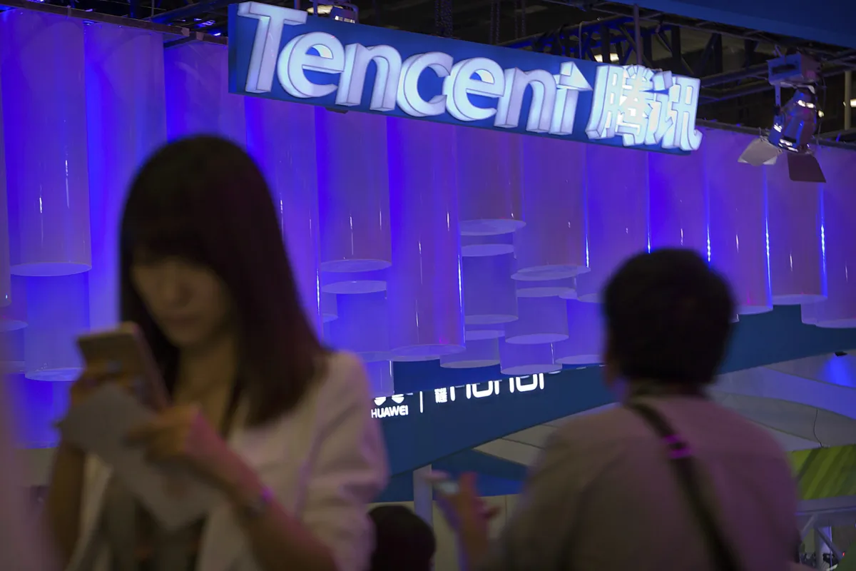 A woman uses her smartphone near a booth for the Chinese Internet company Tencent at the Global Mobile Internet Conference in Beijing in this April 29, 2015 file photo. (AP Photo/Mark Schiefelbein)