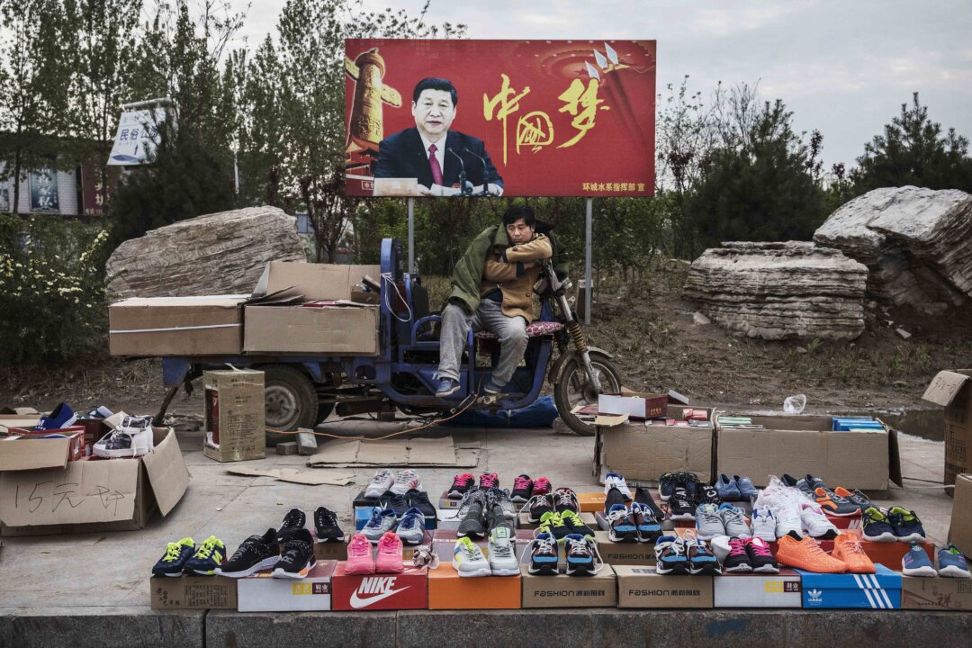 A Chinese vendor sells sneakers and shoes in the street in front of a sign showing Chinese leader Xi Jinping with "China Dream" written on it, in Shijiazhuang, Hebei Province, China, on April 9, 2017. (Kevin Frayer/Getty Images)