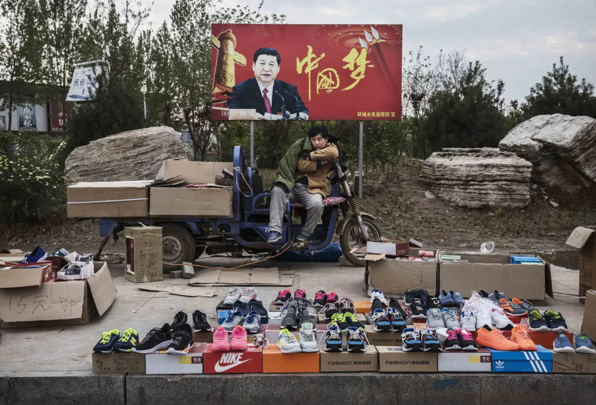A Chinese vendor sells sneakers and shoes in the street in front of a sign showing Chinese leader Xi Jinping with "China Dream" written on it, in Shijiazhuang, Hebei Province, China, on April 9, 2017. (Kevin Frayer/Getty Images)