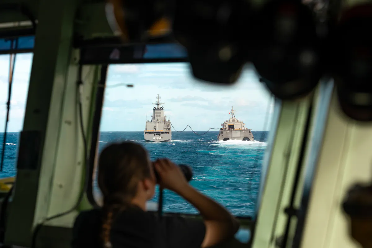 A Sonar operator onboard HMCS Montreal looks out towards His Majesty’s Australian Ship (HMAS) Stalwart (left) and United States Ship (USS) Oakland as they conduct a liquid Replenishment at Sea (RAS) as part of exercise Talisman Sabre while deployed on Operation Projection on July 31, 2023. (Cpl Connor Bennett/ Canadian Armed Forces)