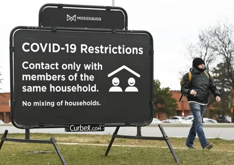 A man walks past a COVID-19 restrictions sign during the pandemic, in Mississauga, Ont., on Dec. 22, 2020. (The Canadian Press/Nathan Denette)