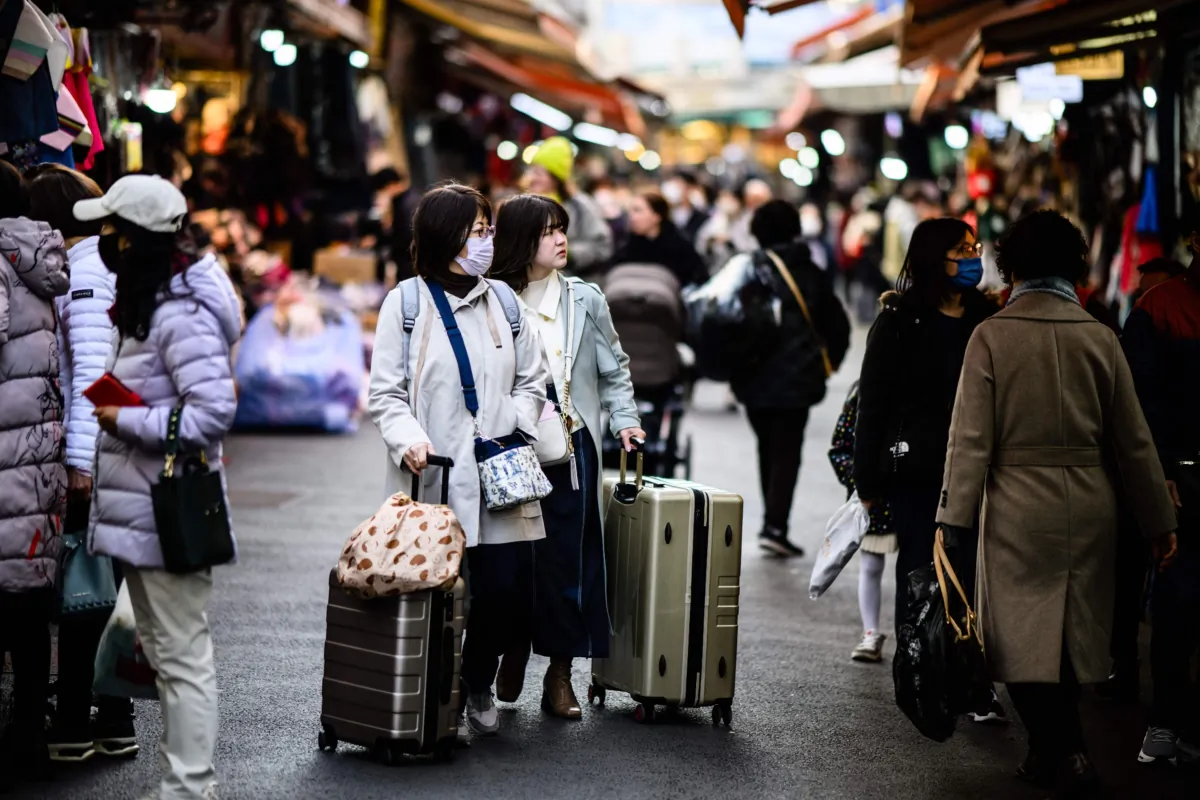 Tourists push luggage past stalls as they visit Namdaemun Market in Seoul on March 13, 2023. (Anthony Wallace /AFP via Getty Images)