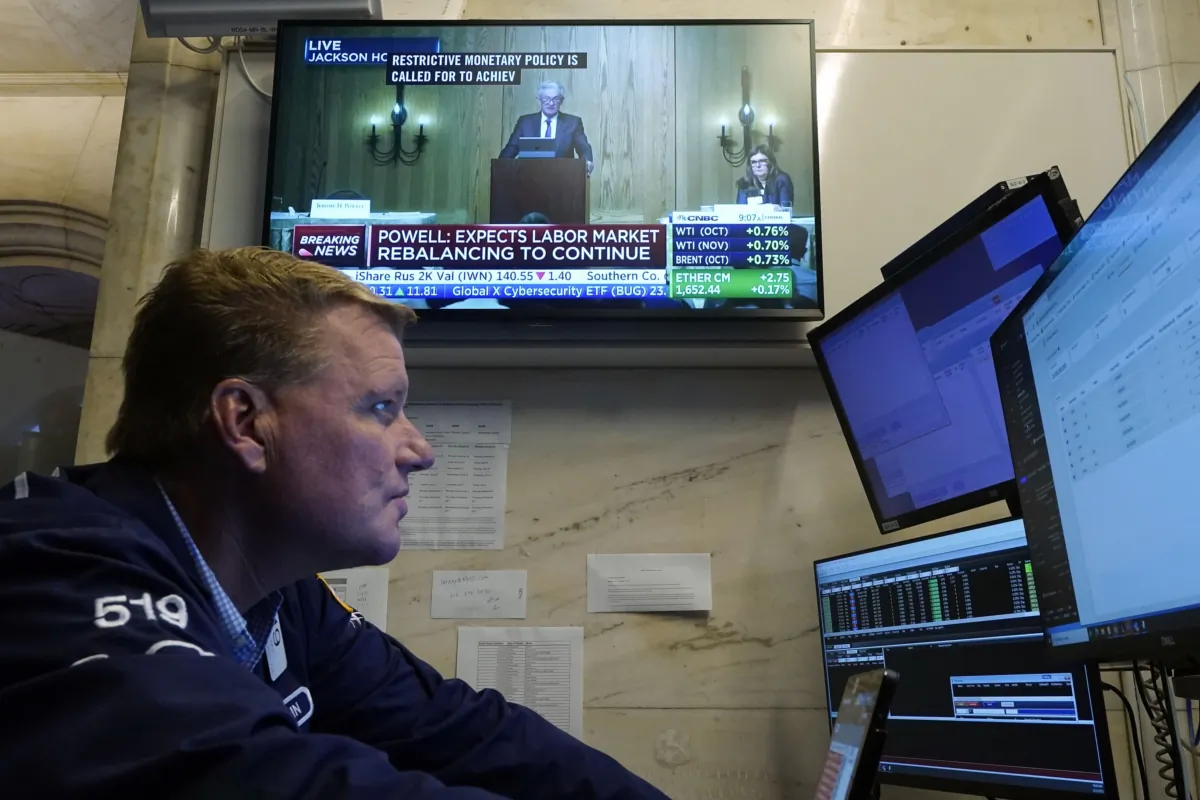 Stock trader John Bowers works on the floor of the New York Stock Exchange on Aug. 25, 2023, as Federal Reserve Chair Jerome Powell's speech is broadcast on a TV screen. (Richard Drew/AP Photo)