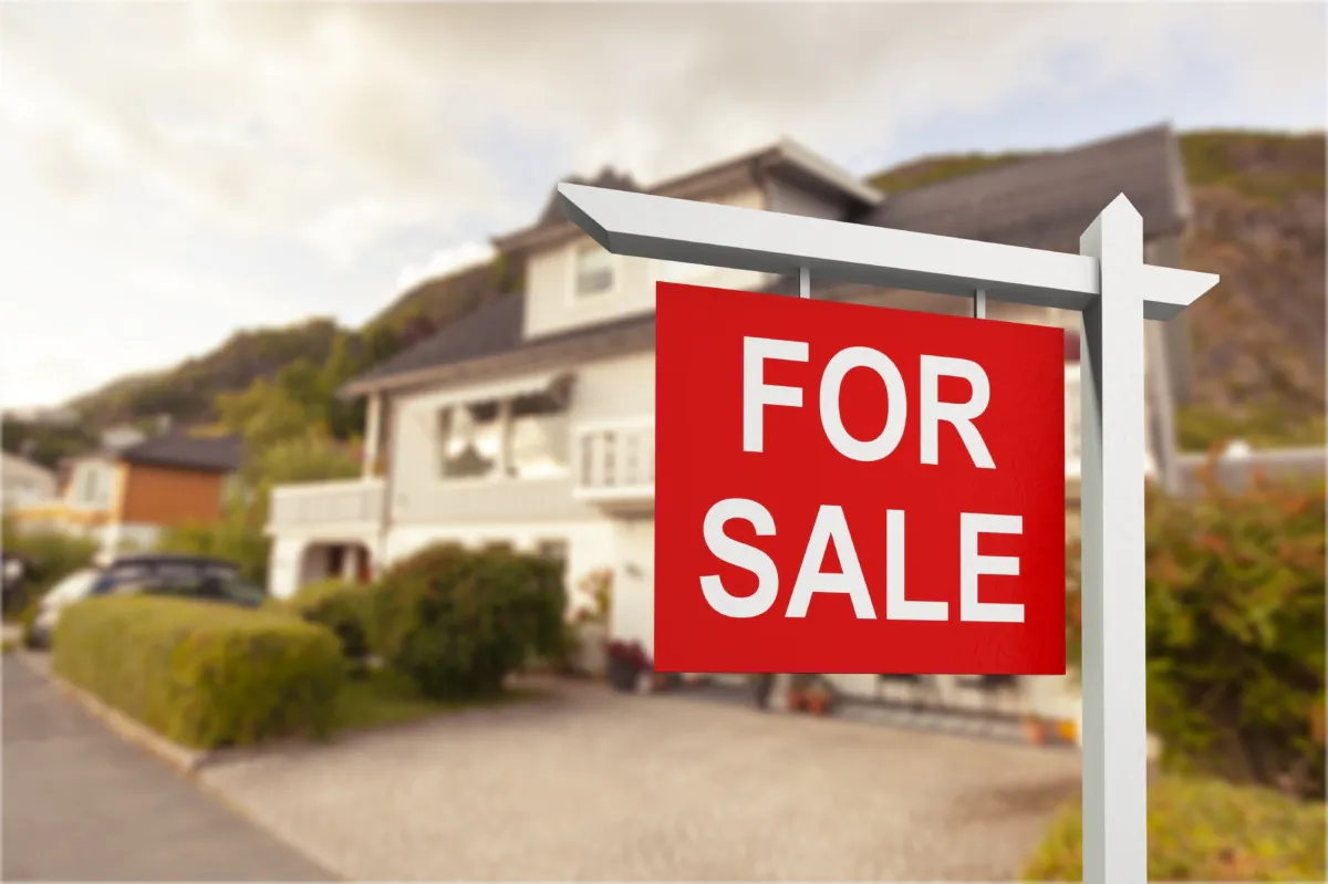Real estate sign in front of new house for sale. (Billion Photos/Shutterstock)