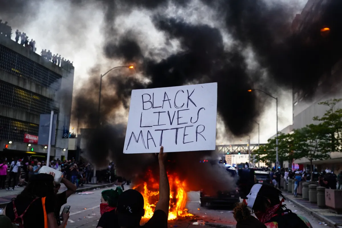A man holds a Black Lives Matter sign as a police car burns in front of him during a protest over the Minneapolis death of George Floyd while in police custody, outside CNN Center in Atlanta on May 29, 2020. (Elijah Nouvelage/Getty Images)