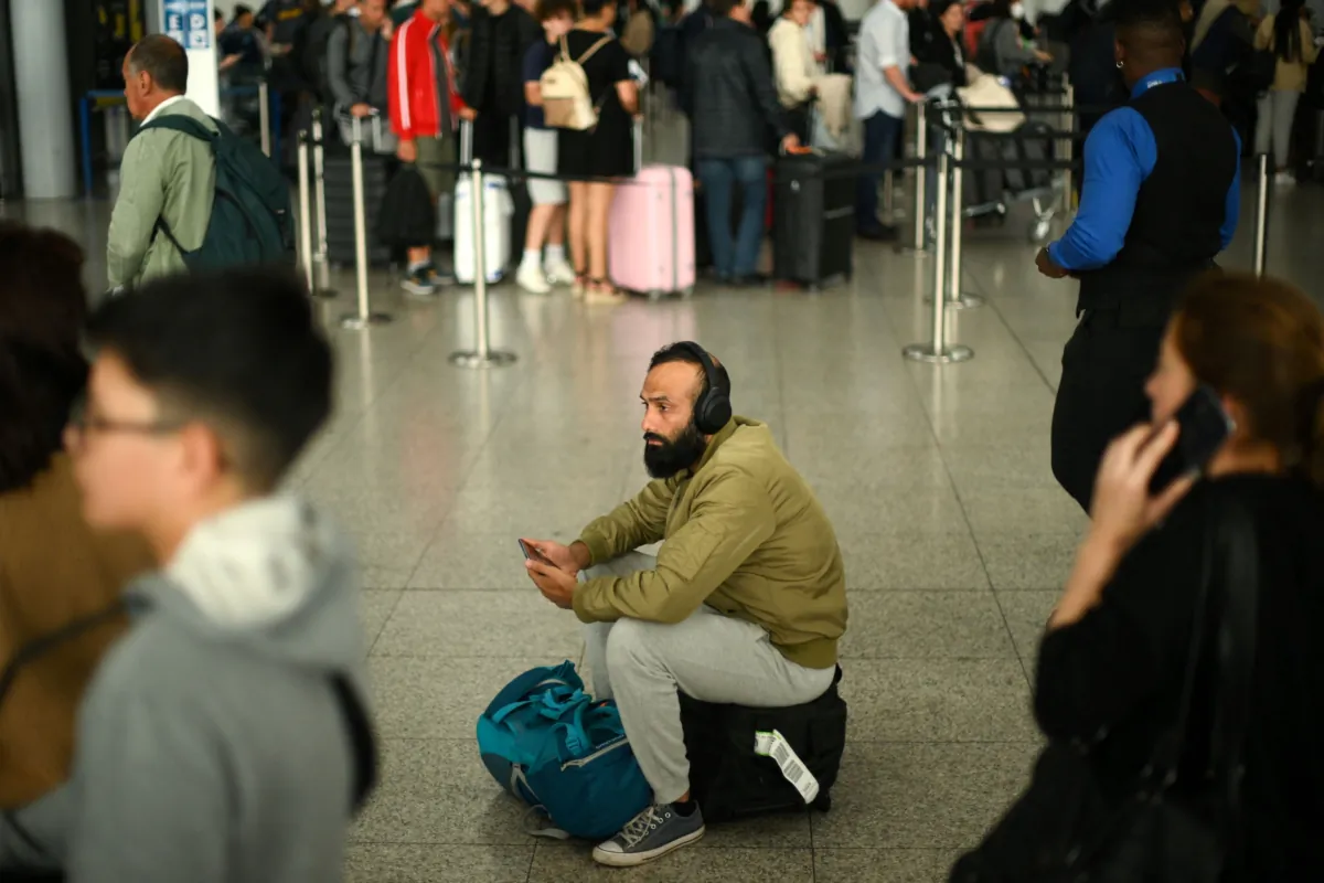 A passenger sits on luggage at Stansted Airport, north of London, after UK flights were delayed over a technical issue, on Aug. 29, 2023. (Daniel Leal/AFP via Getty Images)