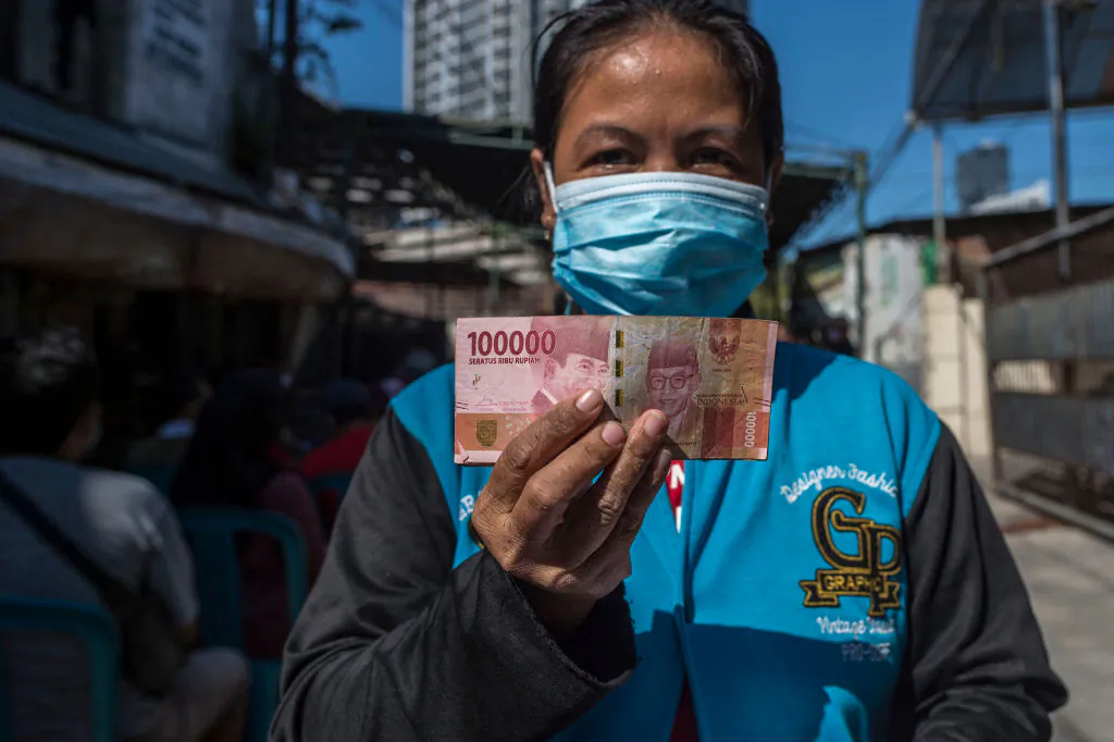 A resident poses with Indonesian rupiah notes, in Surabaya, Indonesia on July 19, 2021. (Juni Kriswanto / AFP via Getty Images)