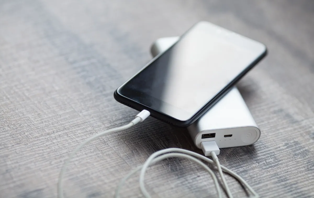 Smartphone charging with power bank on wood board. (LTim/Shutterstock)