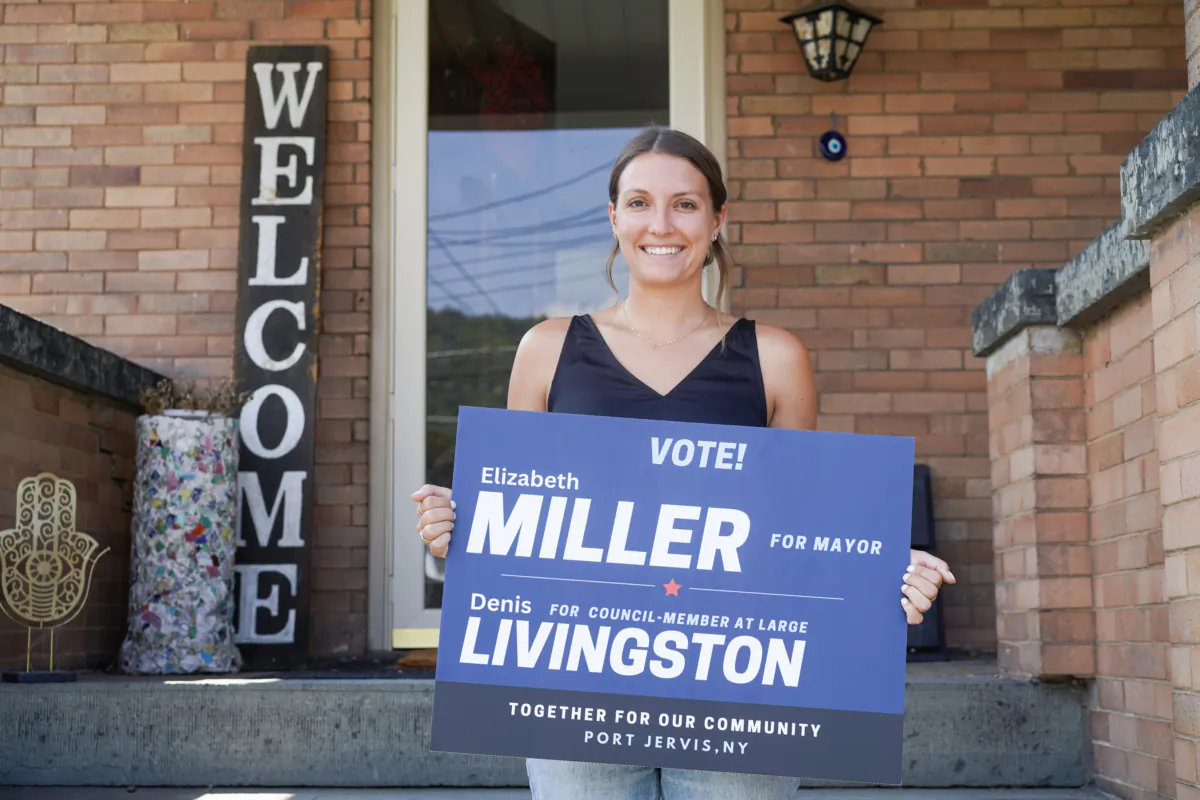 Elizabeth Miller holds up a lawn sign for her mayoral campaign in front of her house in Port Jervis, N.Y., on Sept. 7, 2023. (Cara Ding/The Epoch Times)