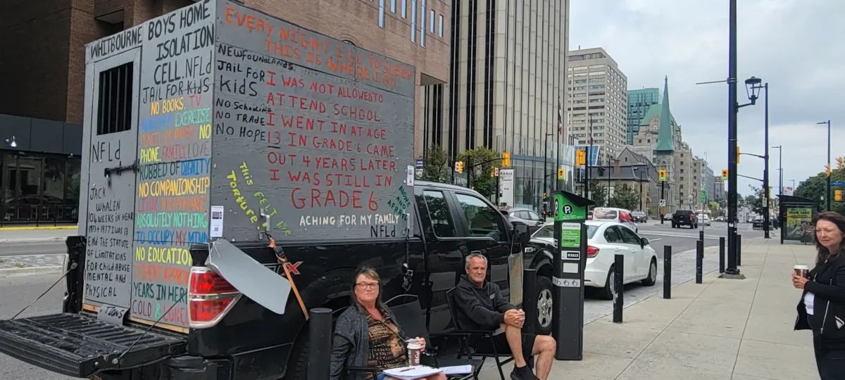 Jack Whalen (C) sits in front of his pickup truck, which holds a replica of the tiny cell in which he spent two years of his life, during a recent protest outside the Ottawa Courthouse. (Matthew Horwood/The Epoch Times).