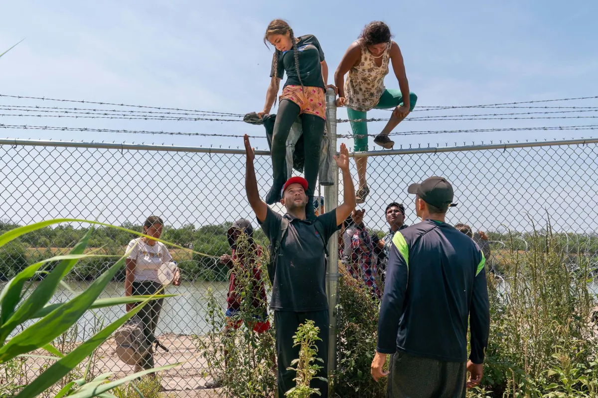 Migrants help each other climb over a barbed wire fence into the U.S. from Mexico, in Eagle Pass, Texas, on Aug. 25, 2023. (Suzanne Cordeiro/AFP/Getty Images)