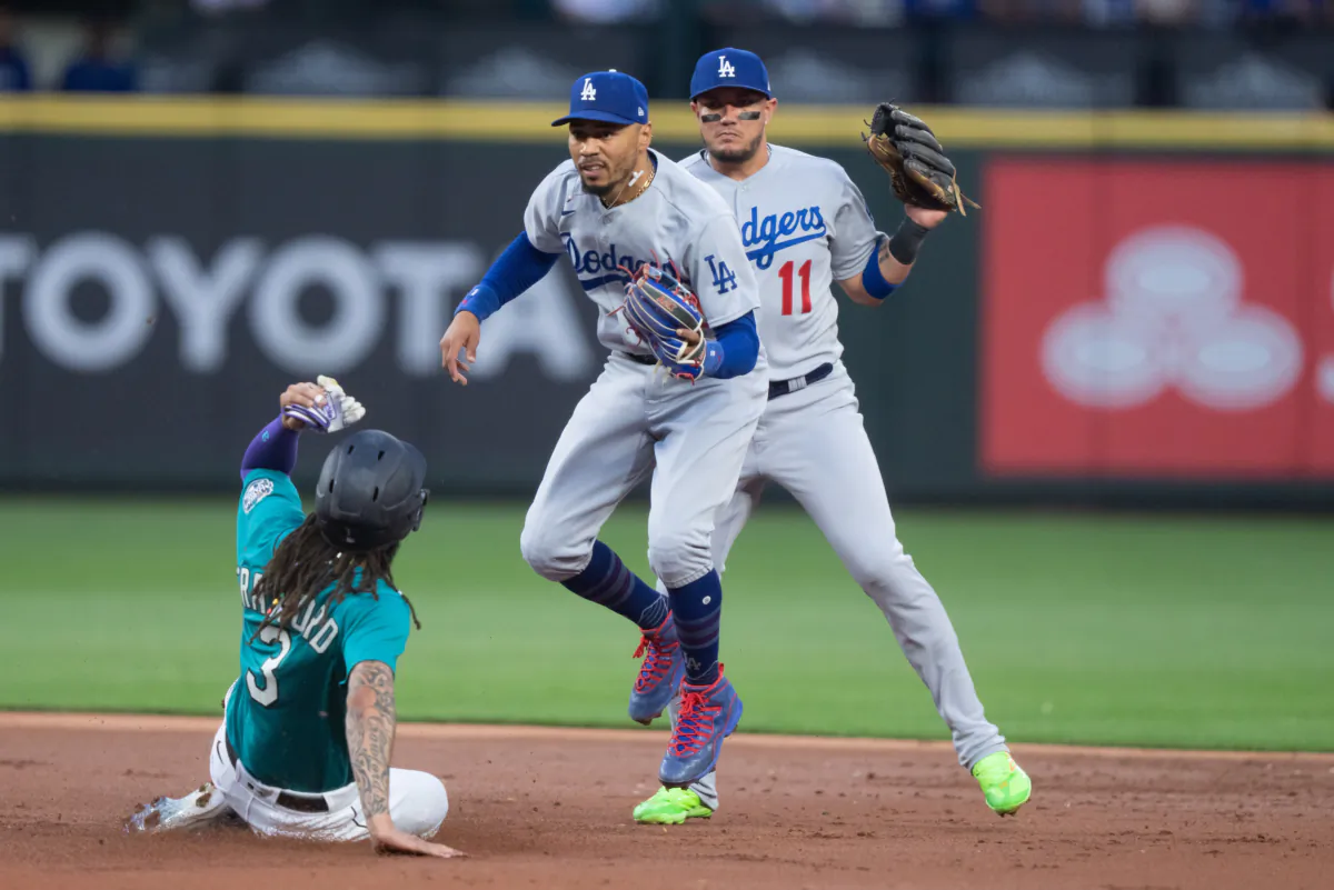Second baseman Mookie Betts (50) of the Los Angeles Dodgers hops out of the way after forcing out J.P. Crawford (3) of the Seattle Mariners at second base, with shortstop Miguel Rojas (11) in background during the first inning of a game at T-Mobile Park in Seattle on Sept. 16, 2023. (Stephen Brashear/Getty Images)