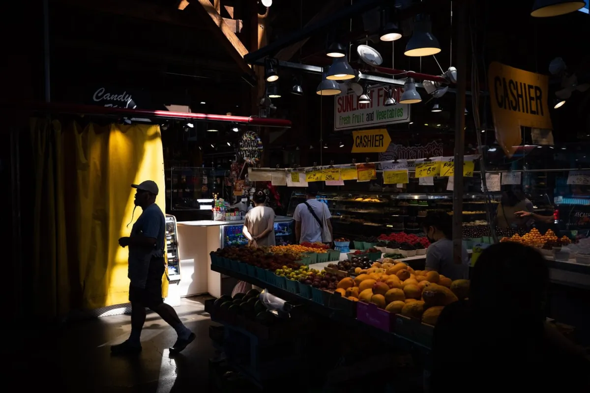 A person is silhouetted as people shop for produce at the Granville Island Market in Vancouver, on July 20, 2022. (The Canadian Press/Darryl Dyck)