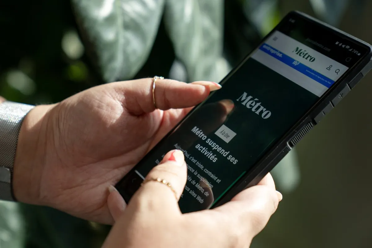 A person holds a phone displaying the home page of Metro Media, which reads in French that the company is suspending activities, in Toronto, on Aug. 11, 2023. (The Canadian Press/Giordano Ciampini)