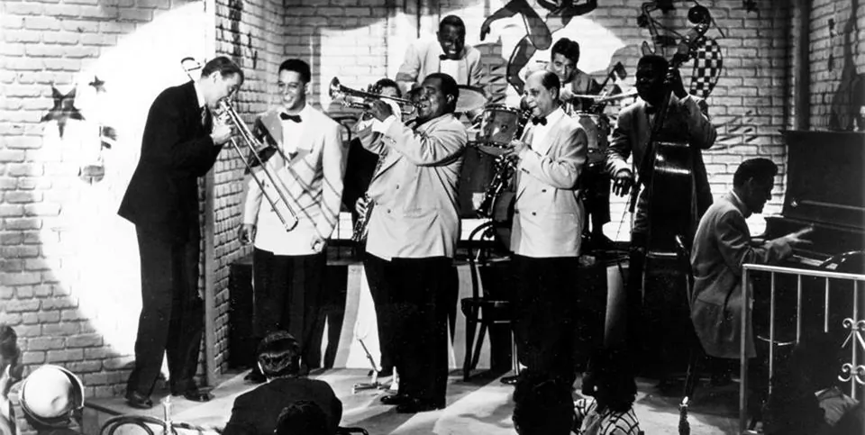 Glenn Miller (James Stewart, L) and Louis Armstrong (2nd R standing) in “The Glenn Miller Story. (Universal-International)