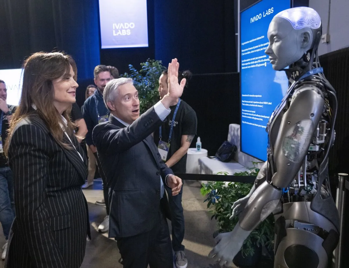 Federal Industry Minister Francois-Philippe Champagne says hello to an AI robot as Helene Desmarais, executive chairwoman, of IVADO Labs looks on at the All In artificial intelligence conference in Montreal on Sept. 27, 2023. (The Canadian Press/Ryan Remiorz)