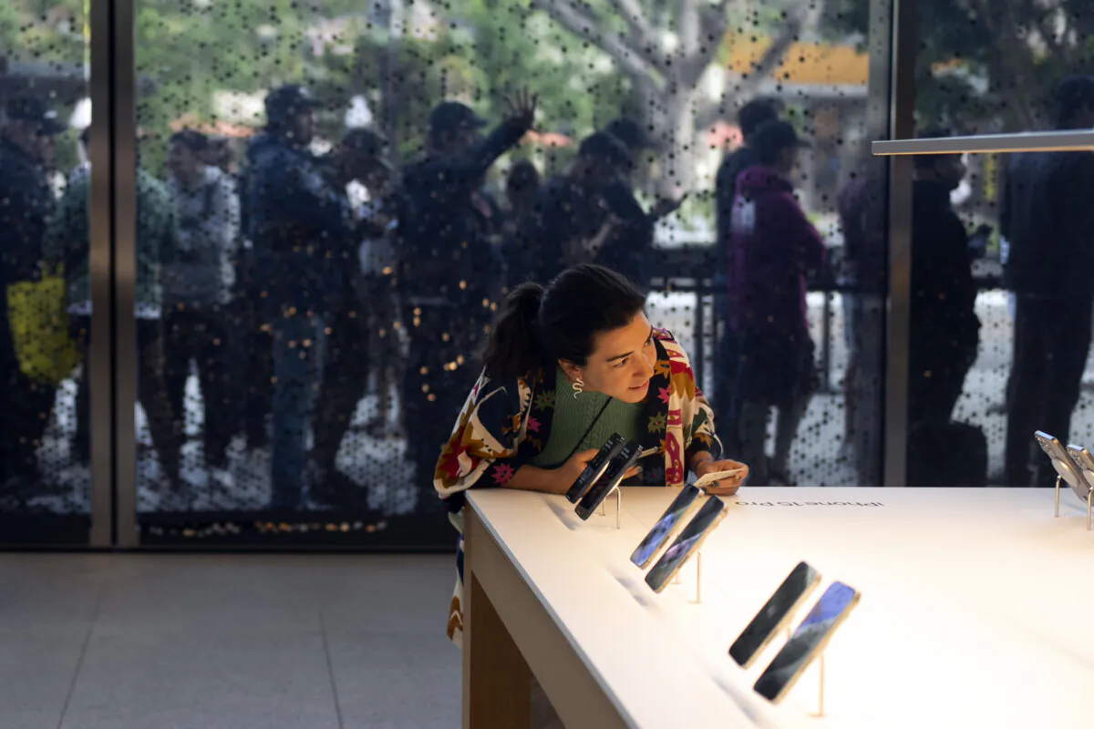 As shoppers wait in the background, a woman looks at Apple's new iPhone 15 at an Apple Store in Los Angeles on Sept. 22, 2023. (Jae C. Hong/AP Photo)