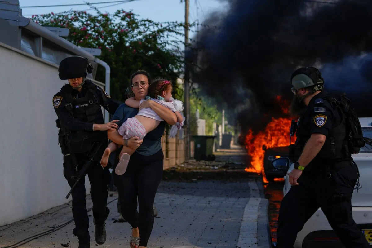Police officers evacuate a woman and a child from a site hit by a rocket fired from the Gaza Strip, in Ashkelon, southern Israel, Oct. 7, 2023. The rockets were fired as Hamas announced a new operation against Israel. (AP Photo/Tsafrir Abayov)