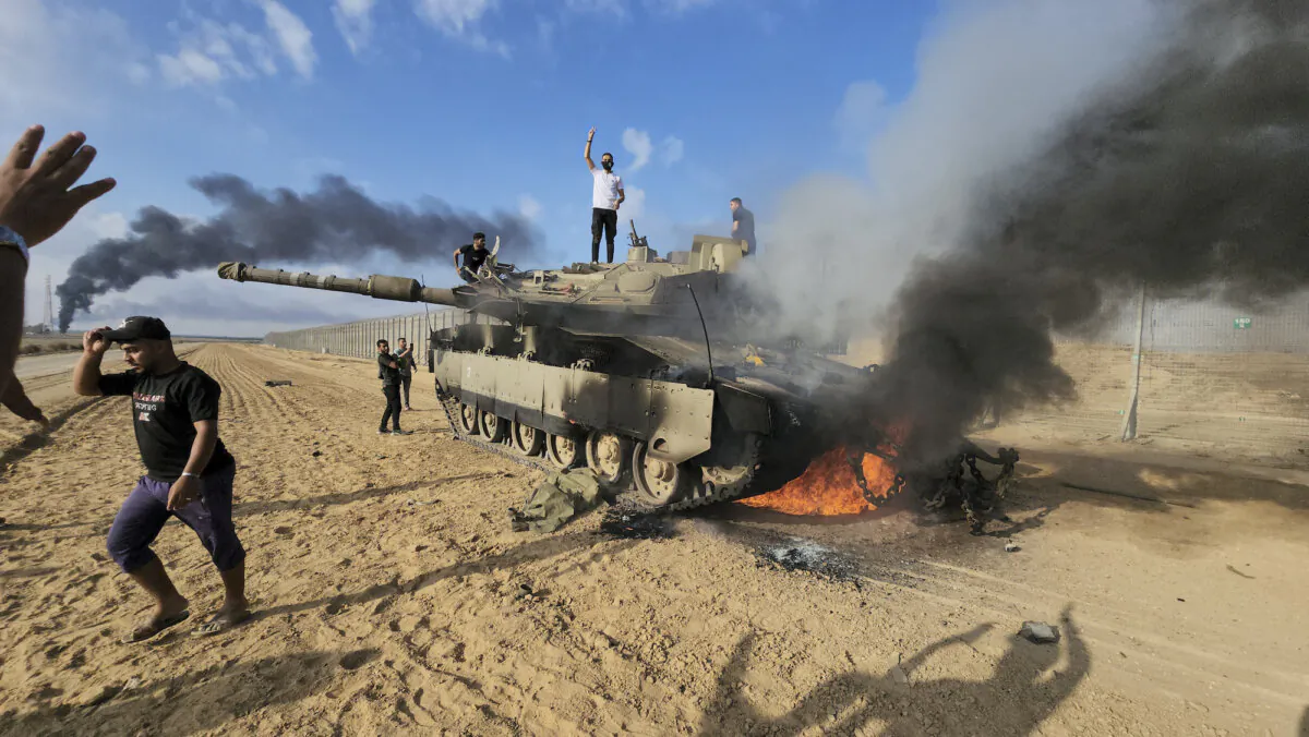Palestinians celebrate by a destroyed Israeli tank at the Gaza Strip fence east of Khan Younis on Oct. 7, 2023.  (AP Photo/Hassan Eslaiah)