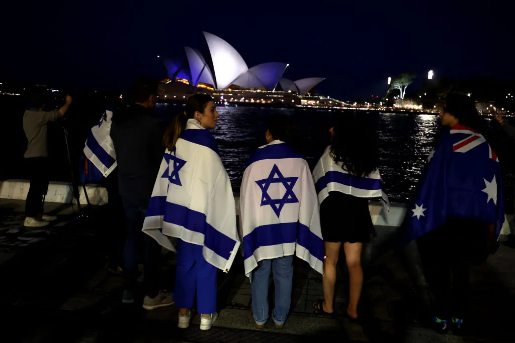 People with Israeli flags watch the Opera House while it is illuminated in blue to show solidarity with Israel in Sydney on Oct. 9, 2023. (DAVID GRAY/AFP via Getty Images)