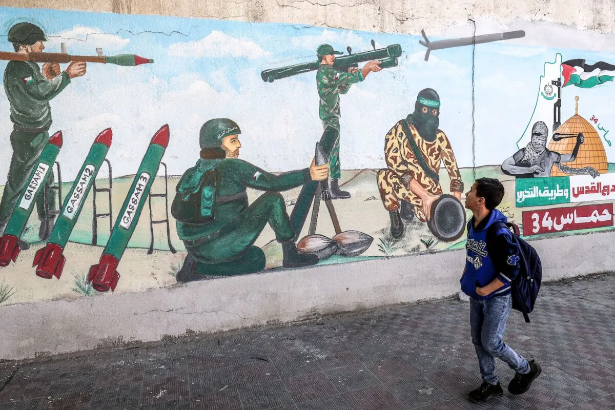 A child walks past a mural depicting soldiers firing rockets as Palestinians mark the 34th anniversary of the founding of the Islamist Hamas movement that rules the Palestinian strip, on Dec. 11, 2021. (Said Khatib/AFP via Getty Images)