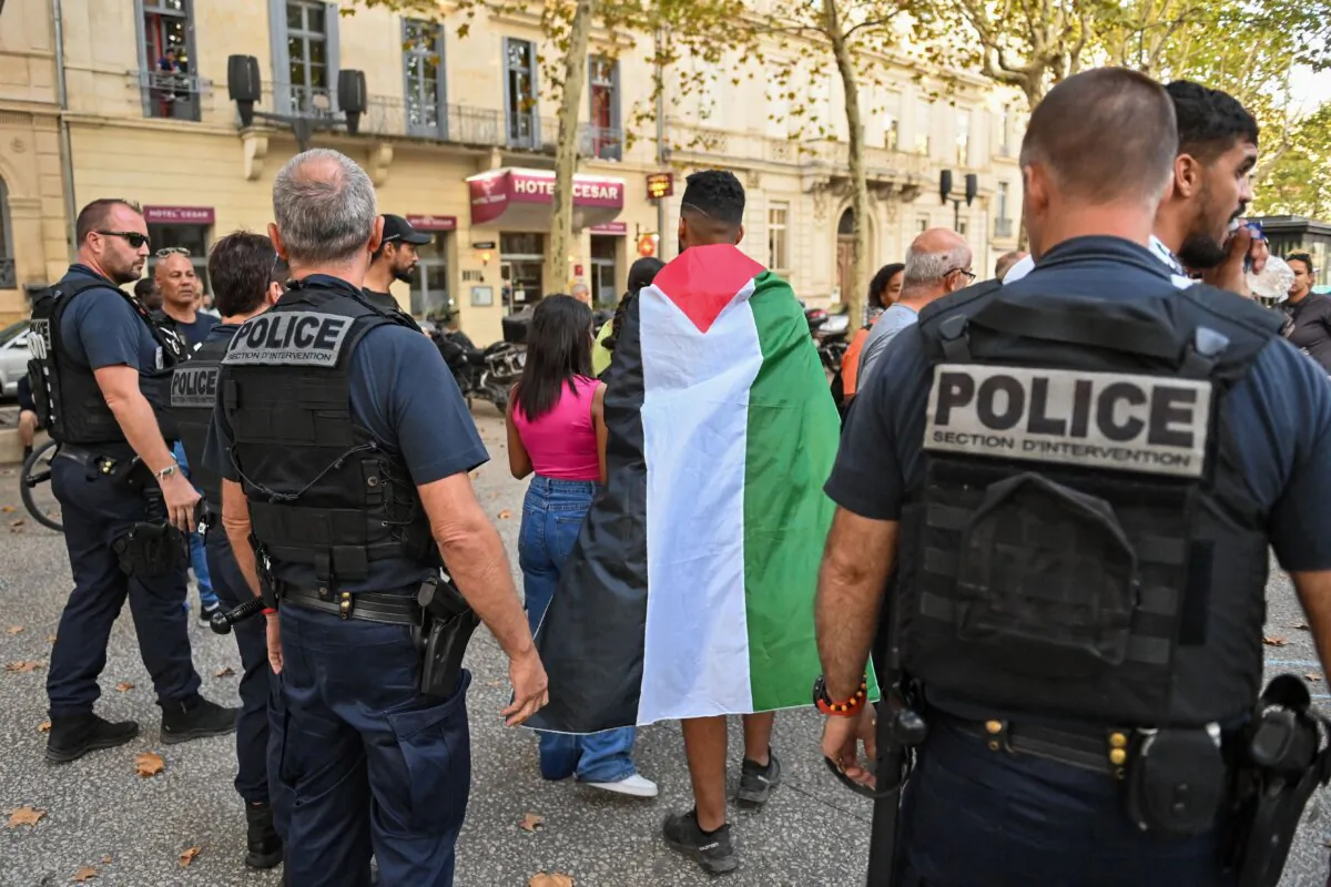 A protestor wrapped in a Palestinian flag walks in front of French police officers during an unauthorized rally in Nimes, southern France, on Oct. 11, 2023 (Sylvain Thomas/AFP via Getty Images)