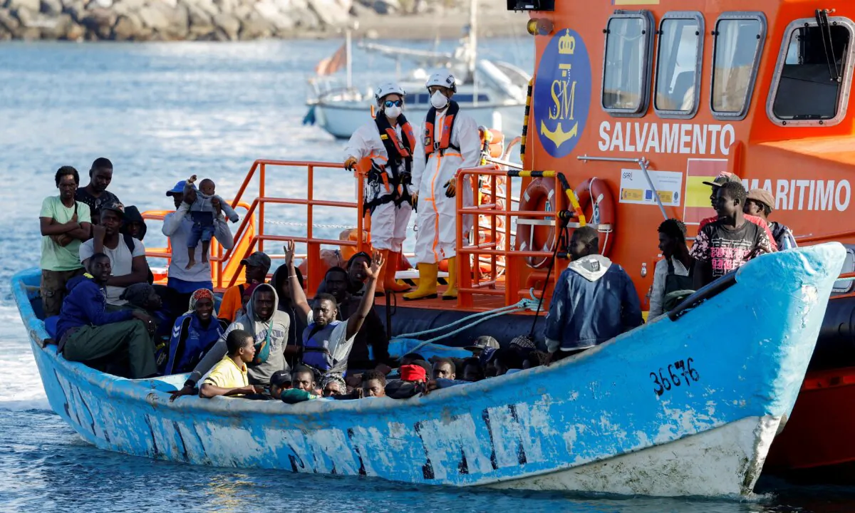 A group of migrants in a wooden boat are towed by a Spanish coast guard vessel to the port of Arguineguin, in the island of Gran Canaria, Spain, on Oct. 12, 2023. (Borja Suarez/Reuters)