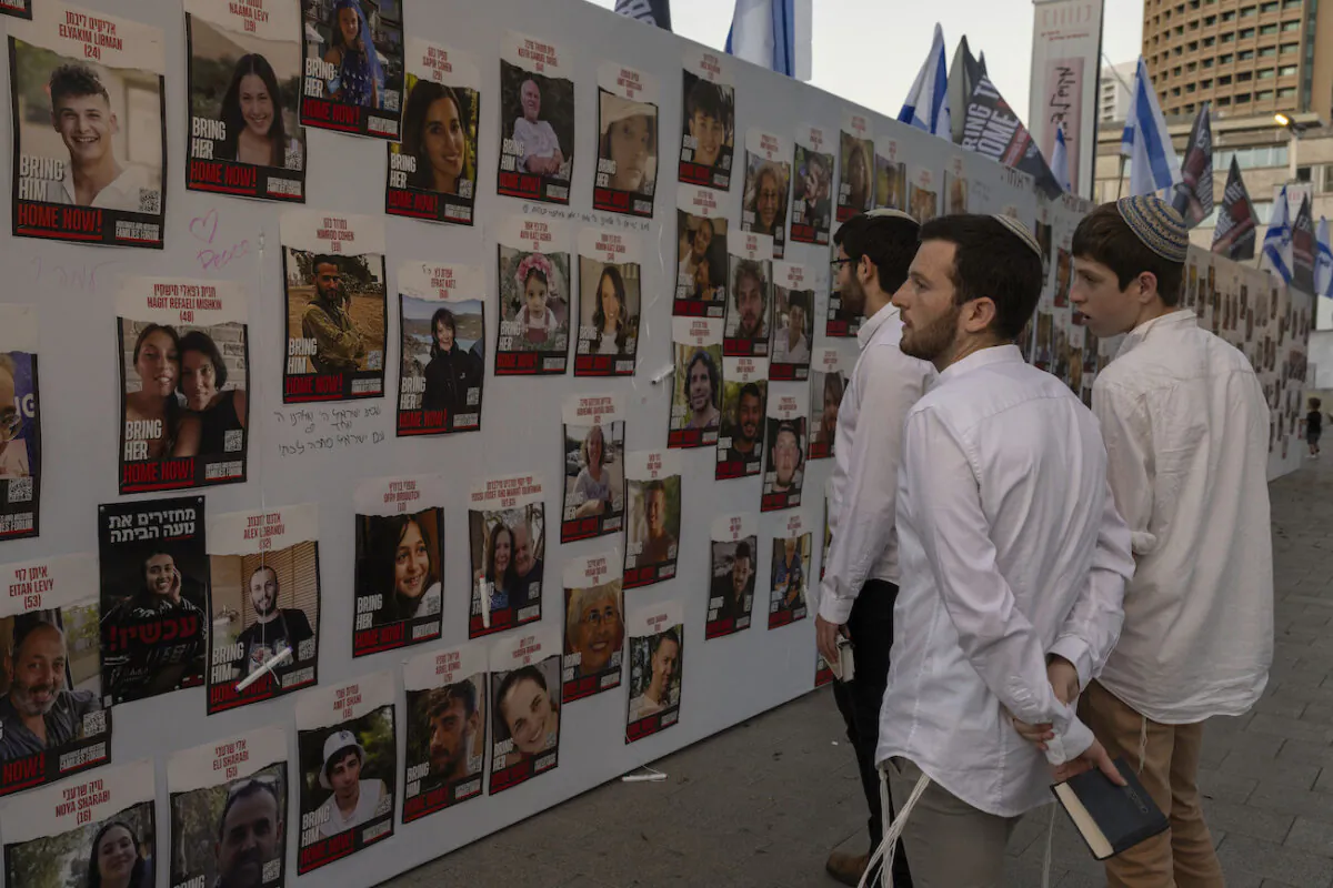 Israeli young men look at photos of Israelis who are missing and held captive in Gaza, displayed on a wall in Tel Aviv, on Oct. 20, 2023. (AP Photo/Petros Giannakouris)