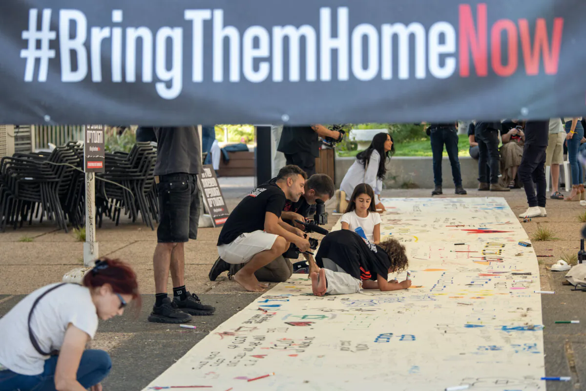 Families of the hostages draw and write messages on a large banner in a special Kabalat Shabbat (welcoming the Shabbat) prayer service next to a Shabbat Dinner table set up in the Tel Aviv museum plaza, with 200 empty seats, representing the hostages and missing people, on Oct. 20, 2023, in Tel Aviv, Israel. (Alexi J. Rosenfeld/Getty Images)