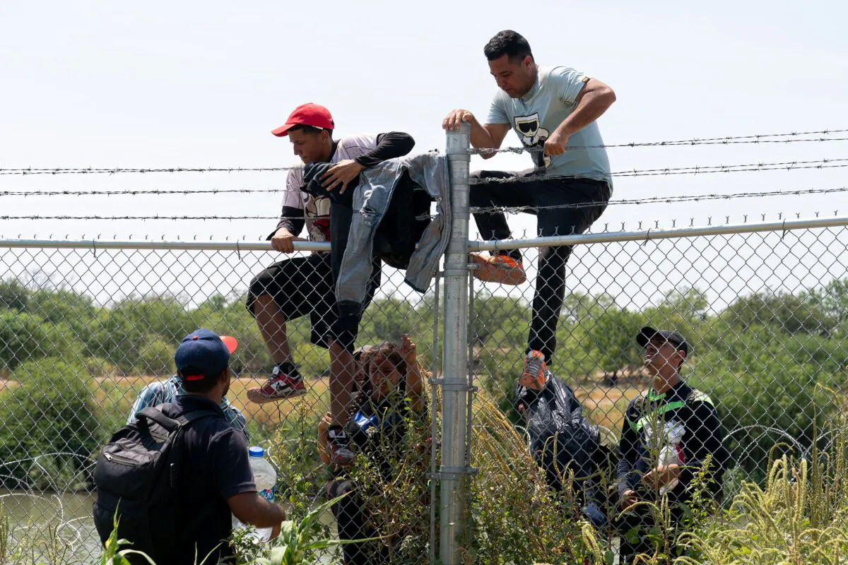 Illegal immigrants climb over the barbed wire fence into the United States from Mexico, in Eagle Pass, Texas, on Aug. 25, 2023. (Suzanne Cordeiro/AFP via Getty Images)